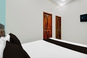 Un dormitorio con cama, dos puertas de madera, un televisor en la pared y un tragaluz.