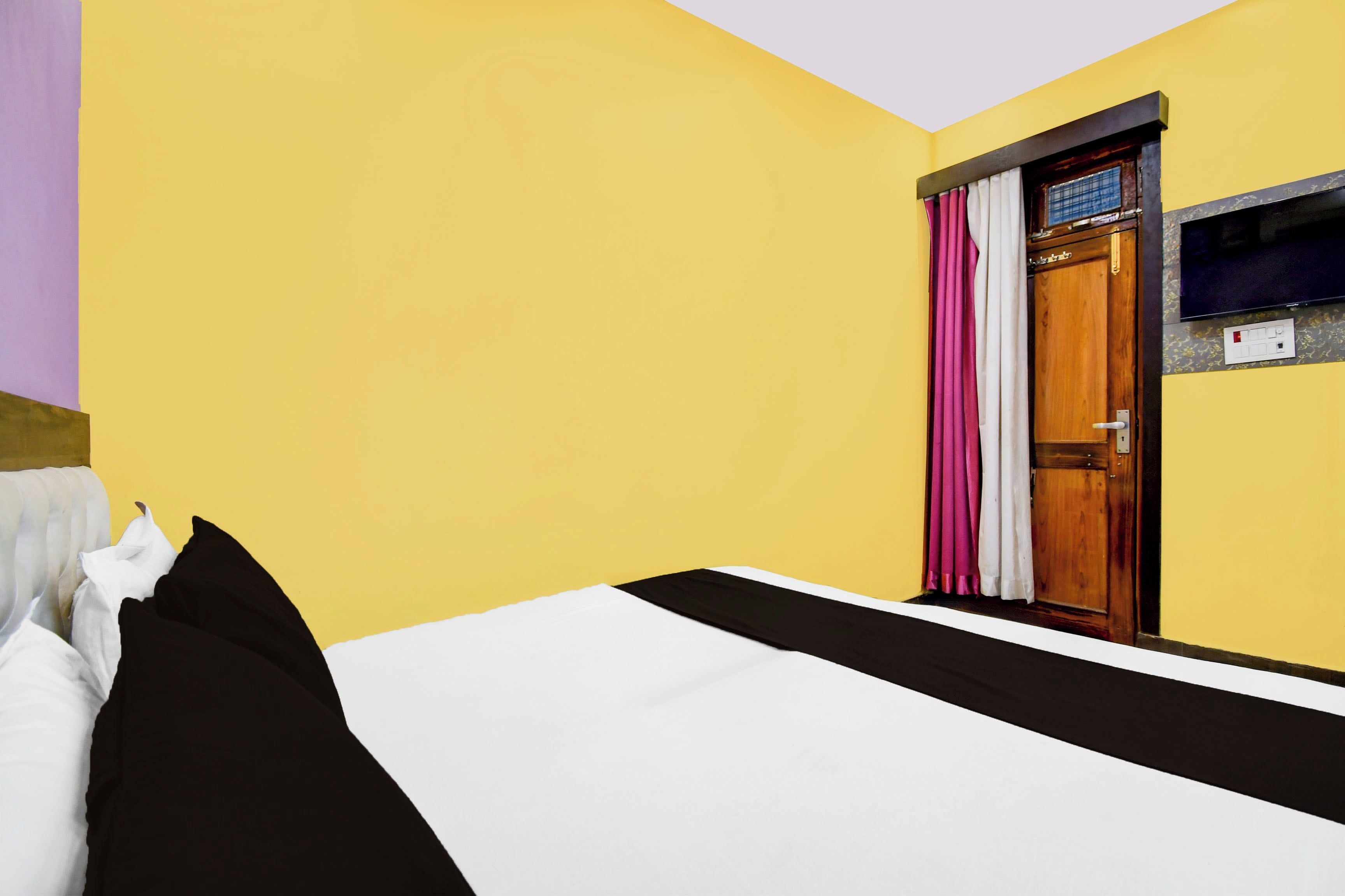A hotel room with a bed, a wooden door, and a television mounted on the wall.