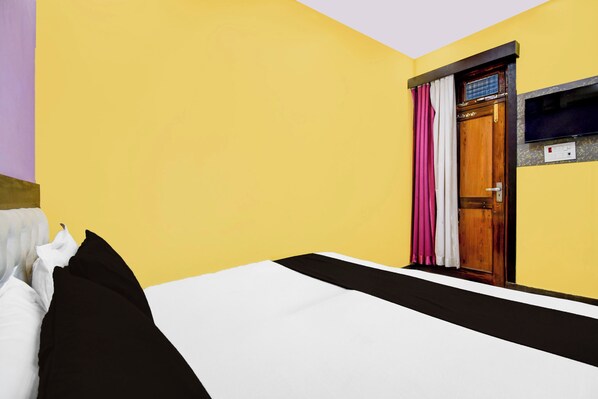 A hotel room with a bed, a wooden door, and a television mounted on the wall.