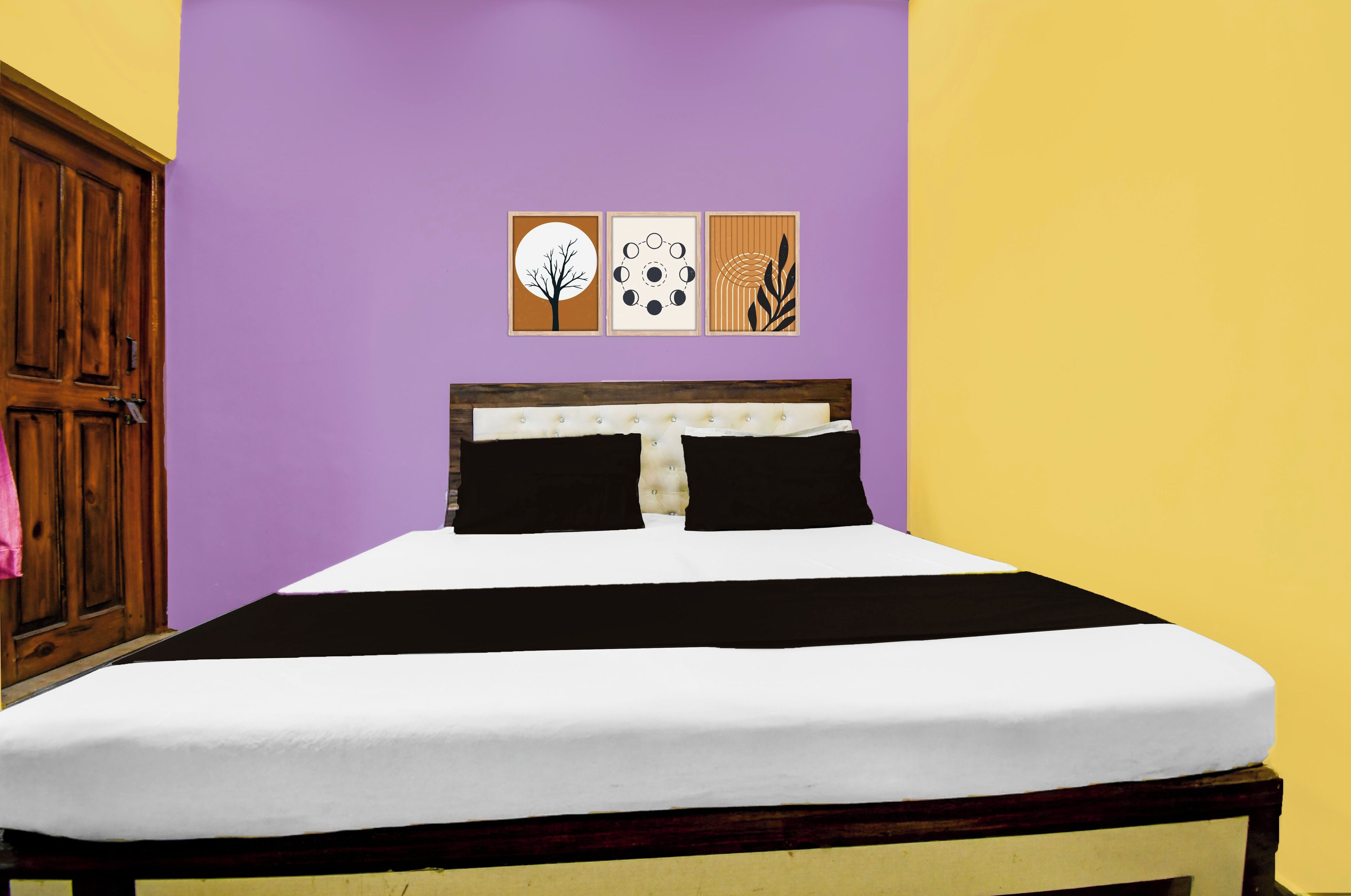 Un letto con materasso bianco e biancheria nera, una testata in legno e una parete viola con tre opere d'arte incorniciate.