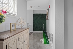A hallway with a wooden cabinet, a framed sign, a green artificial turf, and a wall with a green hedge. - Reunion Resort Retreat with Game Room & Golf Views (Kissimmee)