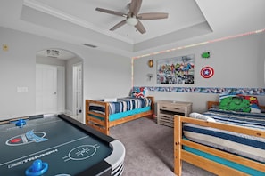 A room with a pool table, two beds, a ceiling fan, and superhero-themed wall art. - Reunion Resort Retreat with Game Room & Golf Views (Kissimmee)