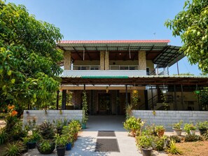 A two-story building with a covered entrance and a garden area with potted plants. - Mango Bite Farmstay (Pollachi)