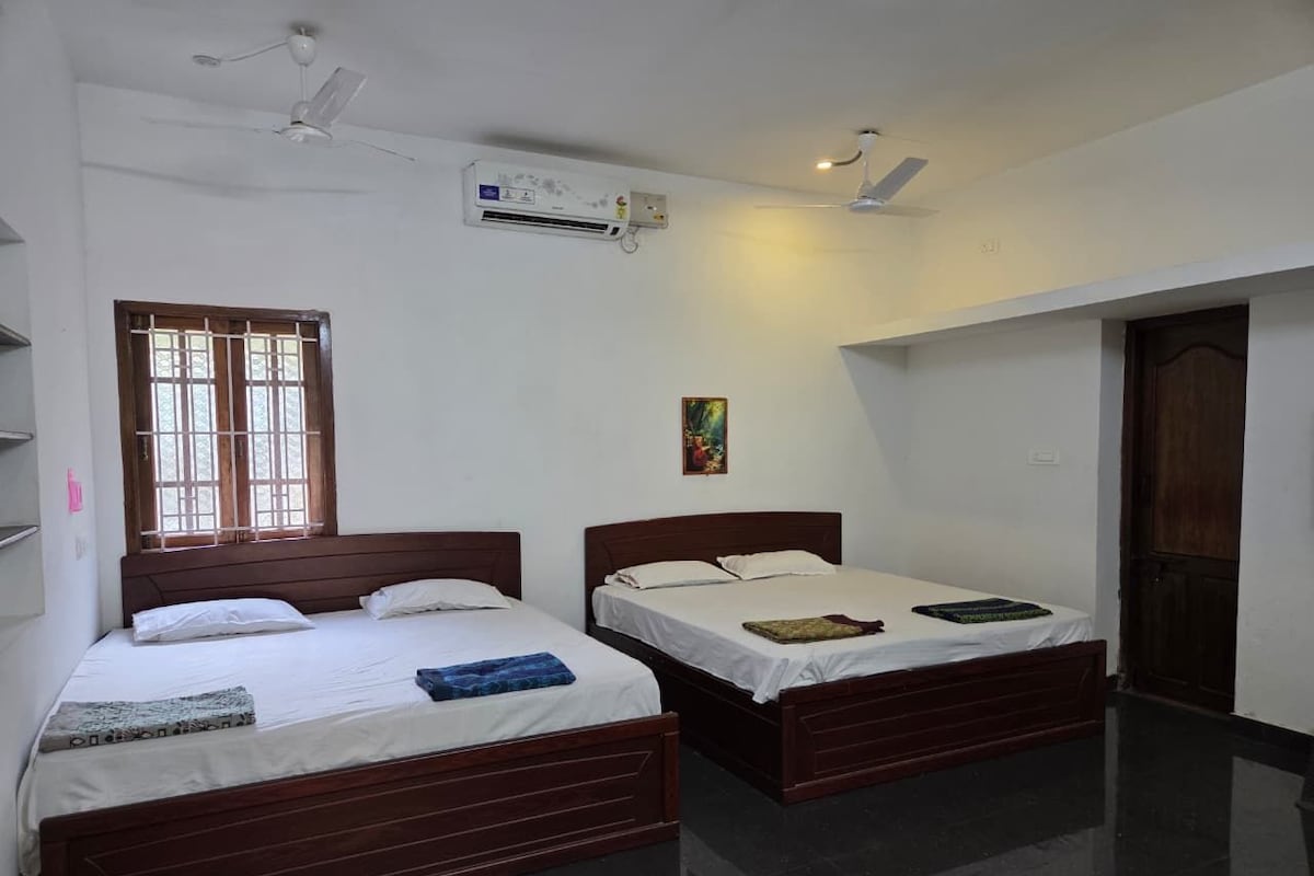 A room with two wooden beds, a window with bars, an air conditioning unit, and a door.