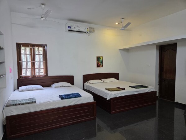 A room with two wooden beds, a window with bars, an air conditioning unit, and a door.
