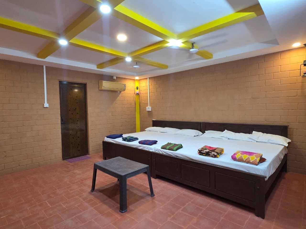 Una habitación con una cama, una mesita, una pared de ladrillo y un techo con vigas amarillas.