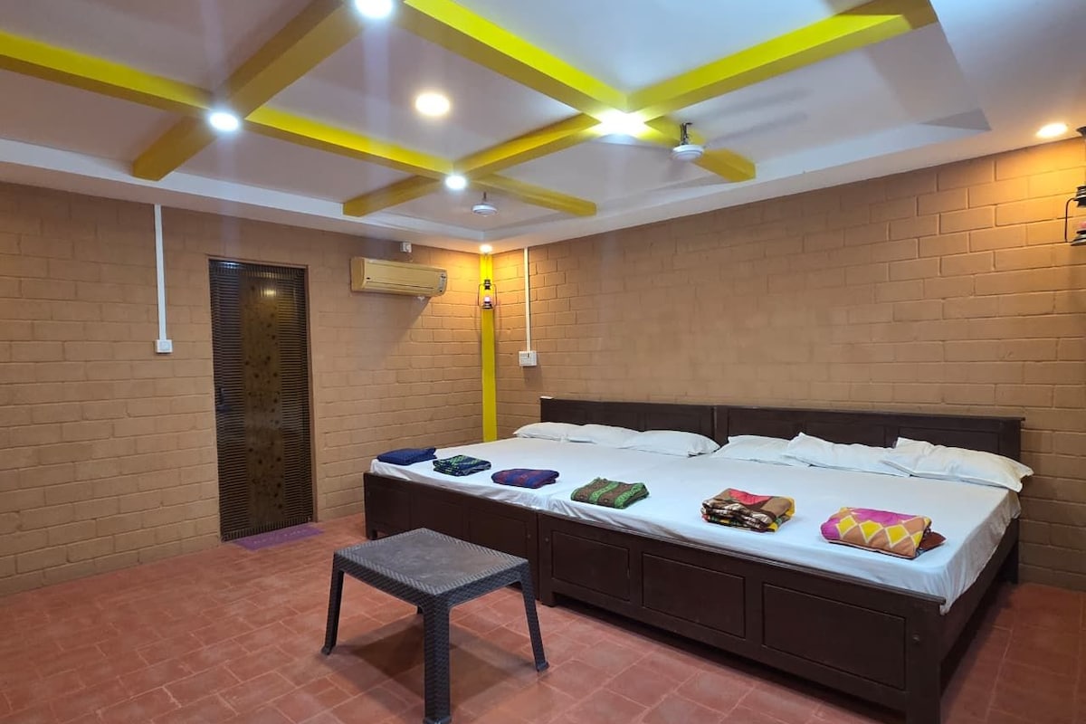 A room with a bed, a small table, a brick wall, and a ceiling with yellow beams.