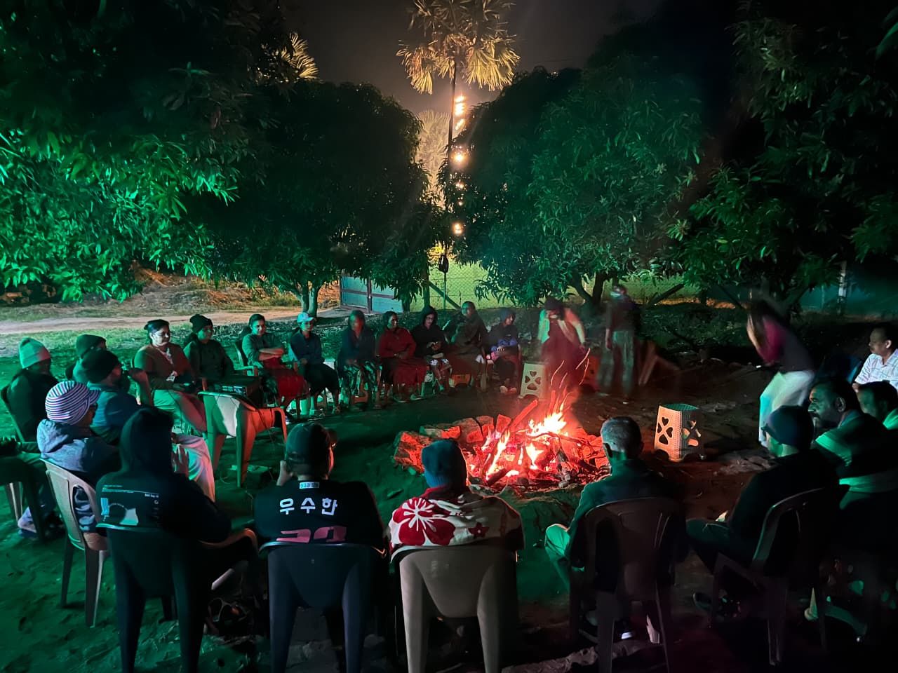 Un grupo de personas sentadas alrededor de una fogata en un entorno natural nocturno.