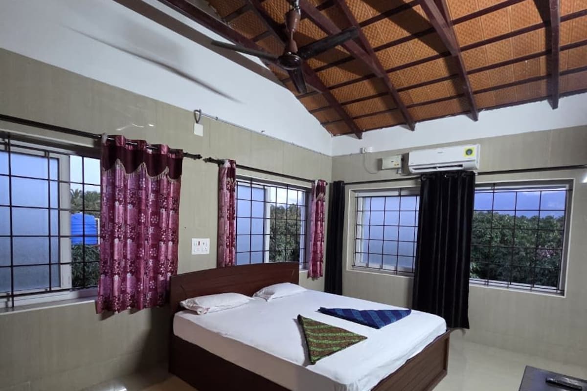 A bedroom with a bed, a small table, and windows with curtains.