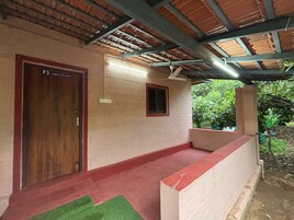 Un porche cubierto con una puerta de madera que dice 'F3 FAMILY COTTAGE', una ventana pequeña y un muro de ladrillo rojo.