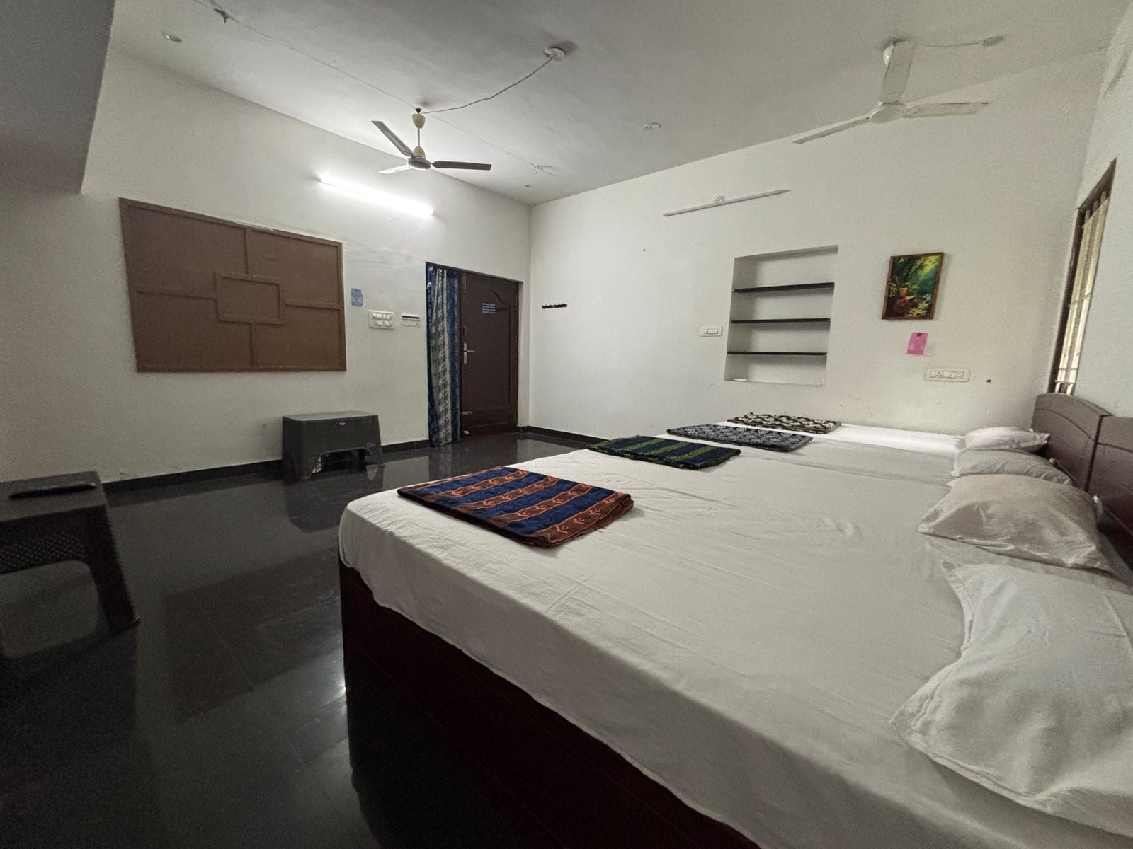 A hotel room with a large bed, a desk, a chair, a wardrobe, a ceiling fan, and a window.