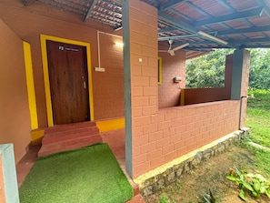 A covered outdoor area with a brick wall, a wooden door labeled 'F2 FAMILY COTTAGE,' and a small grassy patch.