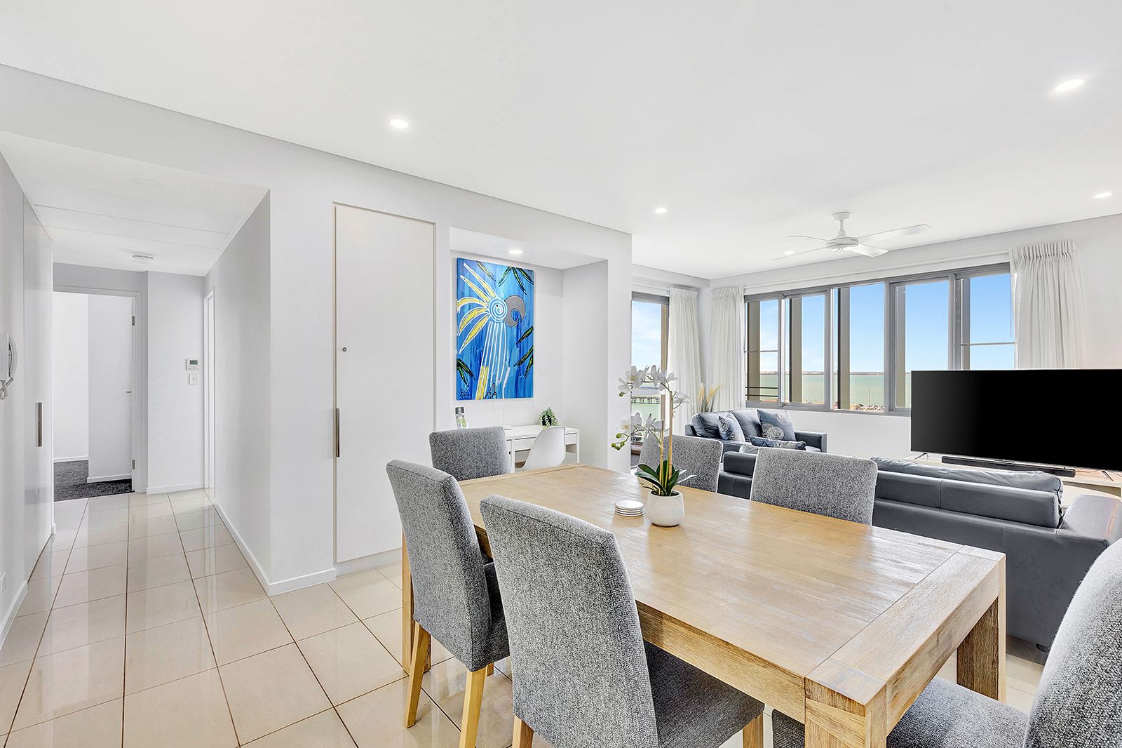 A modern living room with a dining area, a flat-screen TV, and a large window with a view.