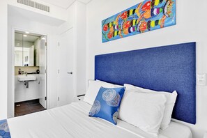 Een hotelkamer met een bed, een badkamer met een wastafel en een kleurrijk abstract schilderij aan de muur.