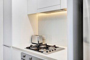 A kitchen with a gas stove, a toaster, and a white countertop. - Deja Blue – Your Serenity Short Stays Darwin Waterfront Escape (Darwin)