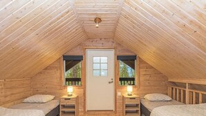 A cozy attic bedroom with two beds, a door with a window, and a small table with a lamp. - Tykkytie cottage by Interhome (Posio)
