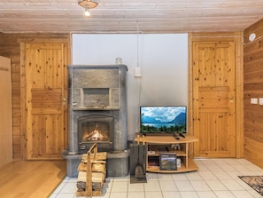 A cozy living room with a stone fireplace, wooden walls, a television, and a small wooden shelf.
