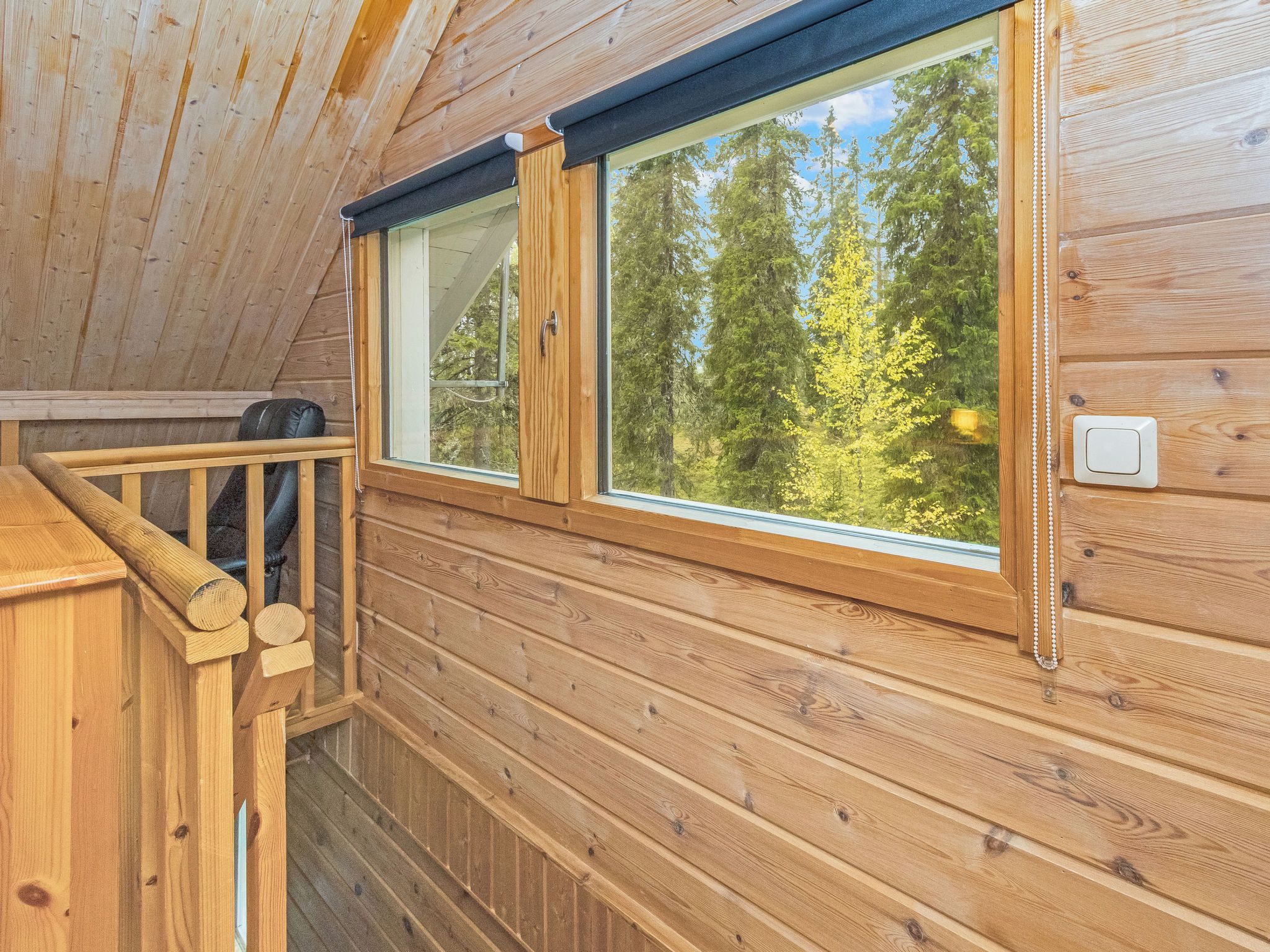 Eine Holzhütte mit Balkon, großen Fenstern und Blick auf Bäume.