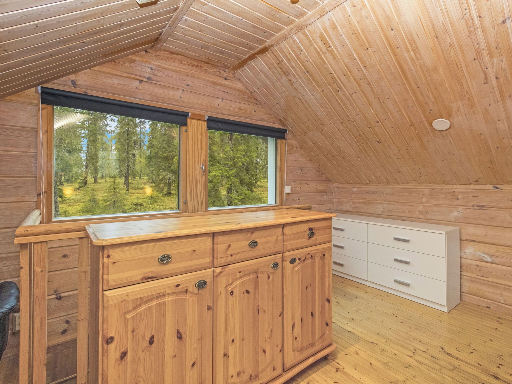 Una baita in legno con un'ampia finestra, mobili in legno e un comò bianco.