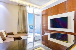 Ein modernes Wohnzimmer mit einem an einer Holzkommode befestigten Flachbildfernseher, einem Glastisch und einer Couch mit Blick ins Freie.