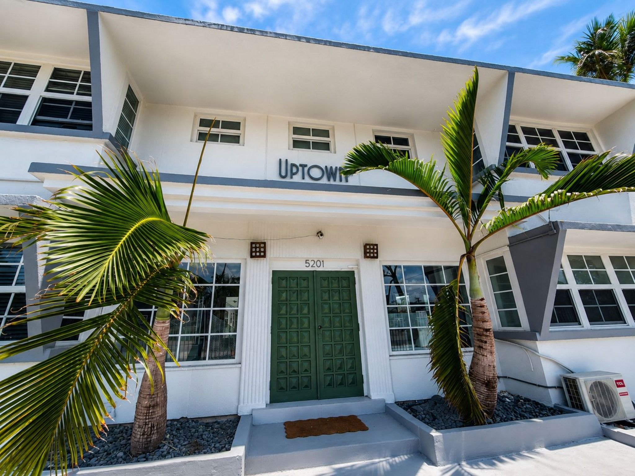 A building with the sign 'UPTOWN' above the entrance, featuring a green door, palm trees, and a white facade.