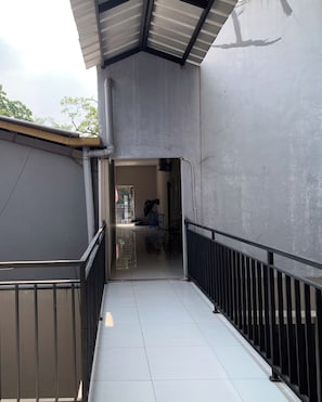 A corridor with a tiled floor, metal railings, and a view into a room with a door and a window.