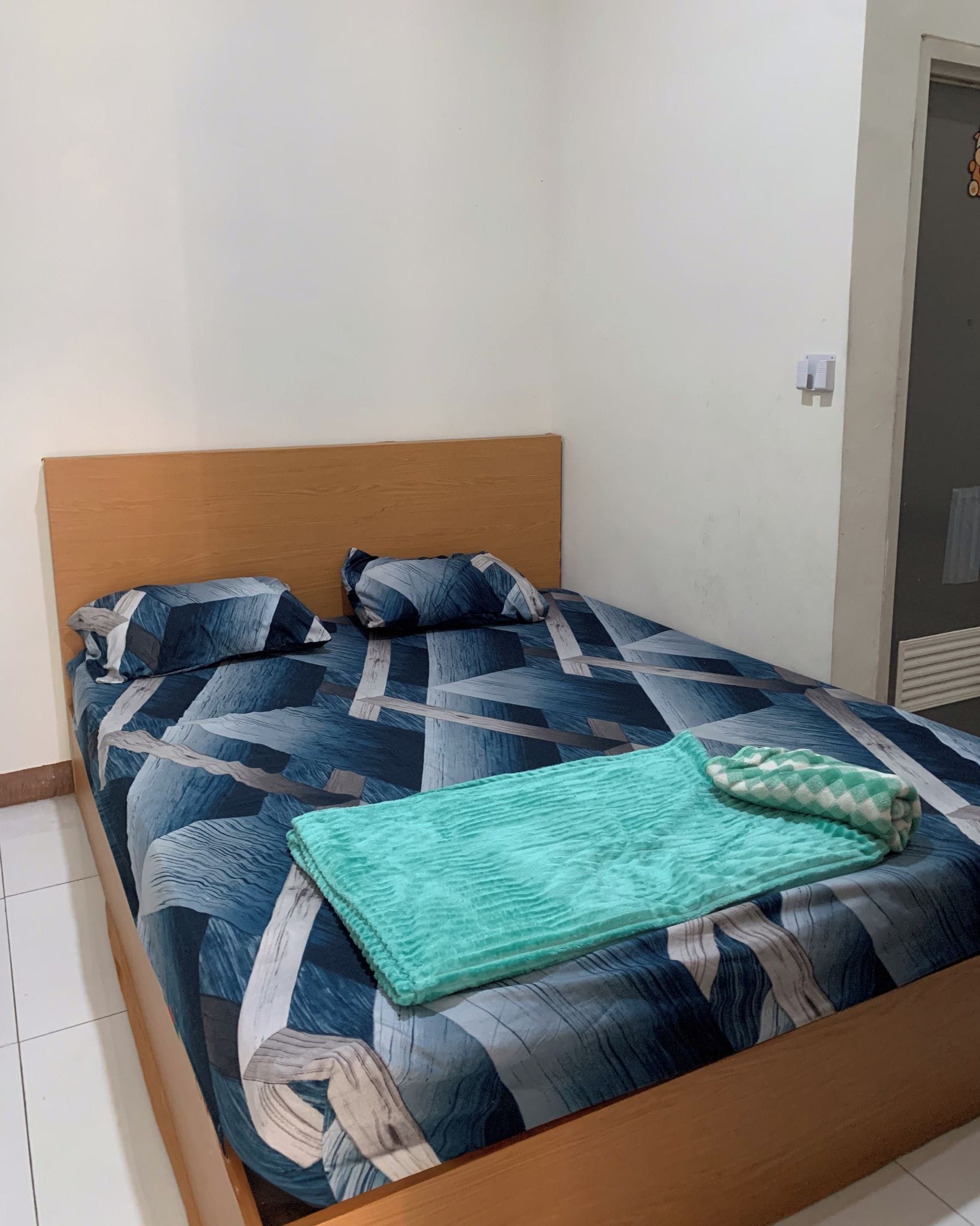 Ein Einzelbett mit Holz Kopfteil, zwei Kissen und einer grünen Decke.
