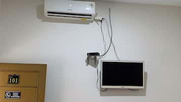 Una habitación con un aire acondicionado blanco, un televisor montado y una puerta con un cartel que indica el número de habitación 101.