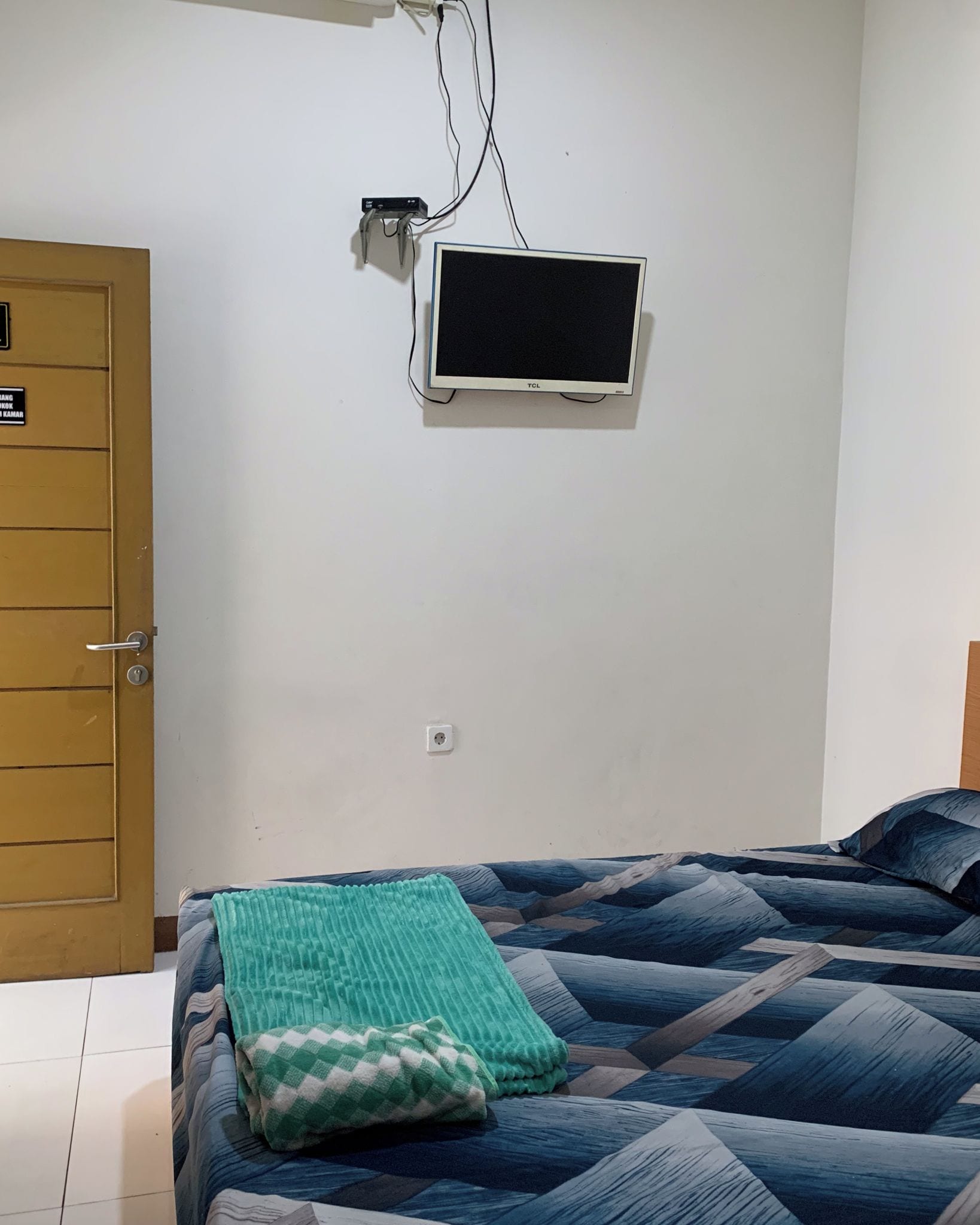 A room with a bed, a wall-mounted TV, and a door.