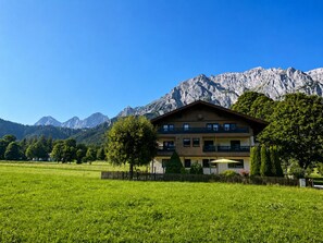 A two-story building with a balcony, surrounded by a green field and mountains in the background. - Vrbo Property (Ramsau am Dachstein)