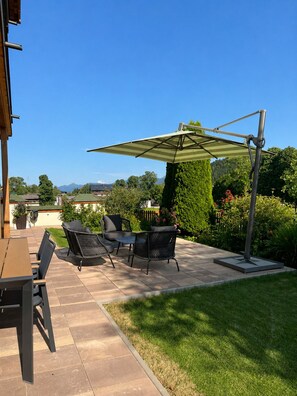 An outdoor patio with a table and chairs, a large umbrella, and a view of the surrounding landscape. - Vrbo Property (Ramsau am Dachstein)