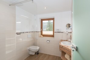 A bathroom with a toilet, a sink, a mirror, and a window. - Vrbo Property (Ramsau am Dachstein)