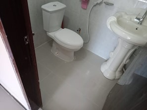 Kylpyhuone, jossa on wc, pesuallas ja ovi, joka johtaa toiseen huoneeseen.