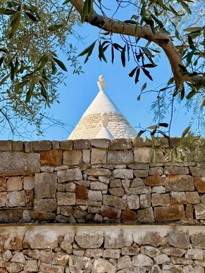 A stone wall with a white conical structure in the background. - Trullo Ostro - Fable Retreats - Chic Puglia Style (Ostuni)