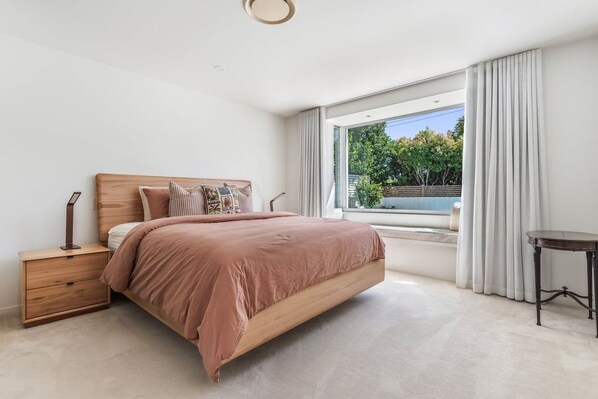 Un dormitorio moderno con una cama grande, mesitas de noche, una ventana con cortinas y vistas al exterior.