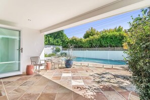 Un patio moderno al aire libre con piscina, zona de estar y puerta de vidrio que da a una habitación.