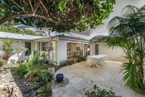 Una casa moderna con patio, mobiliario exterior y diversas plantas.