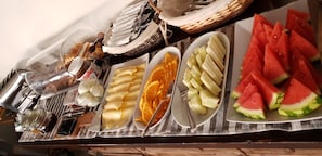 En buffetbord med forskellige spiser, herunder brød, ost, frugt og tilbehør.