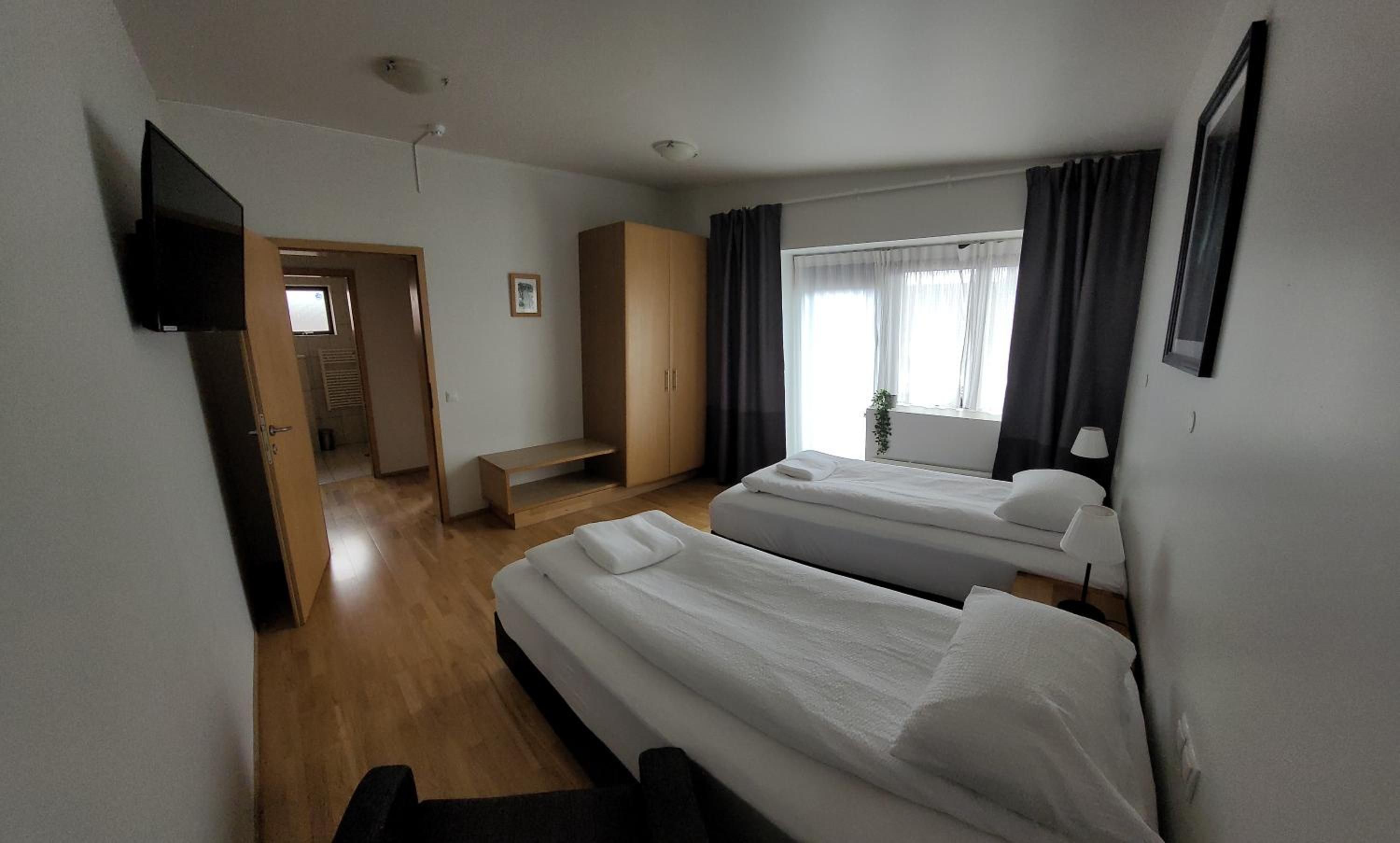 A hotel room with two beds, a TV, a desk, and a window with curtains.