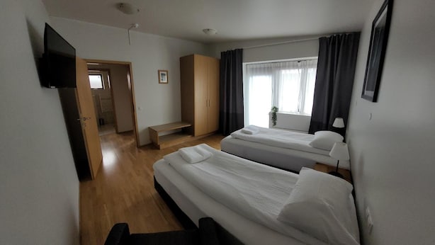 Ein Hotelzimmer mit zwei Betten, einem Fernseher, einem Schreibtisch und einem Fenster mit Vorhängen.