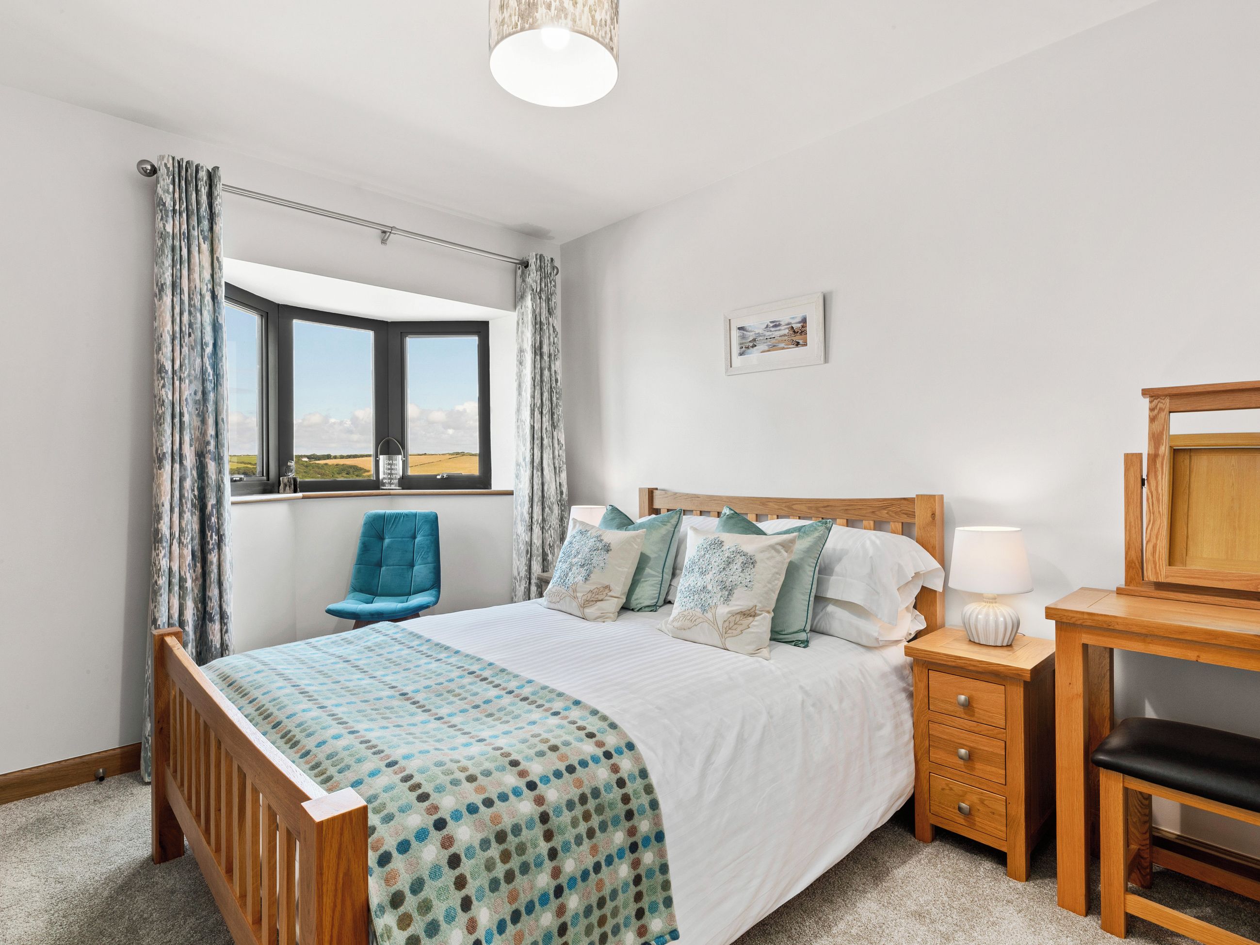A bedroom with a bed, a desk, a chair, a window with curtains, and a picture on the wall.