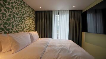 A hotel room with a bed, curtains, a window, and a wall with a leaf pattern.