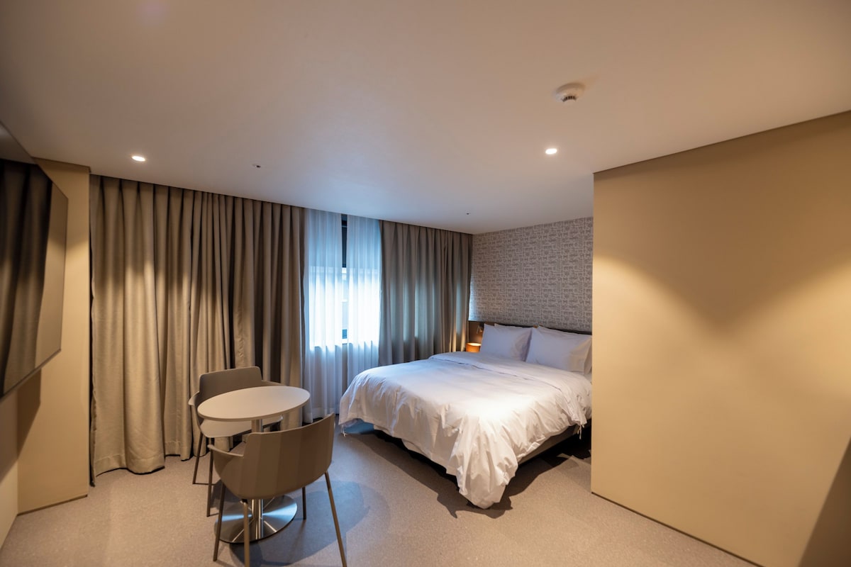 A hotel room with a bed, a round table, two chairs, and a window with curtains.
