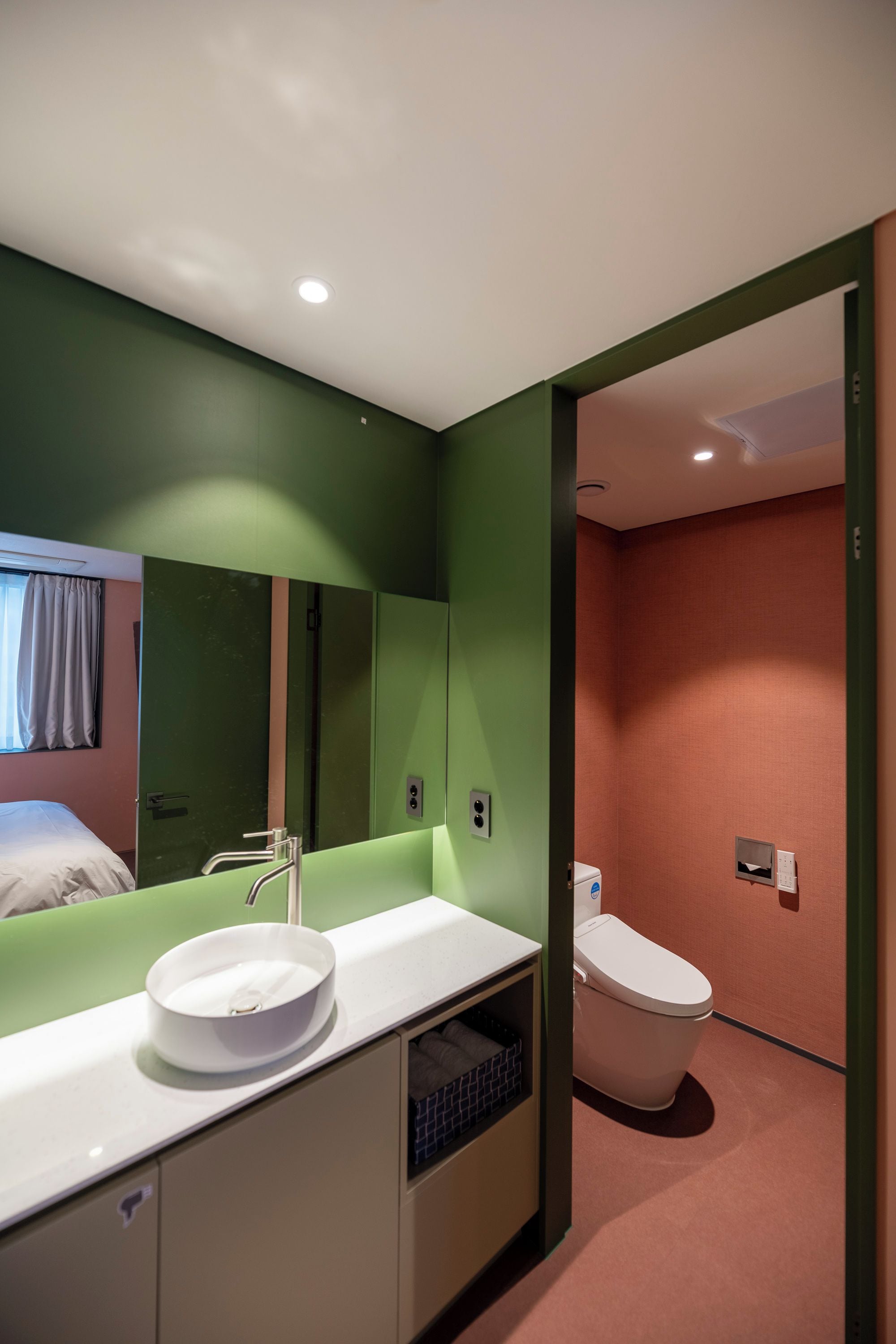 A modern bathroom with a green wall, a white sink, and a toilet.