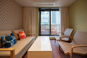 A hotel room with a sofa, two armchairs, a small table, and a balcony with a view of tall buildings.