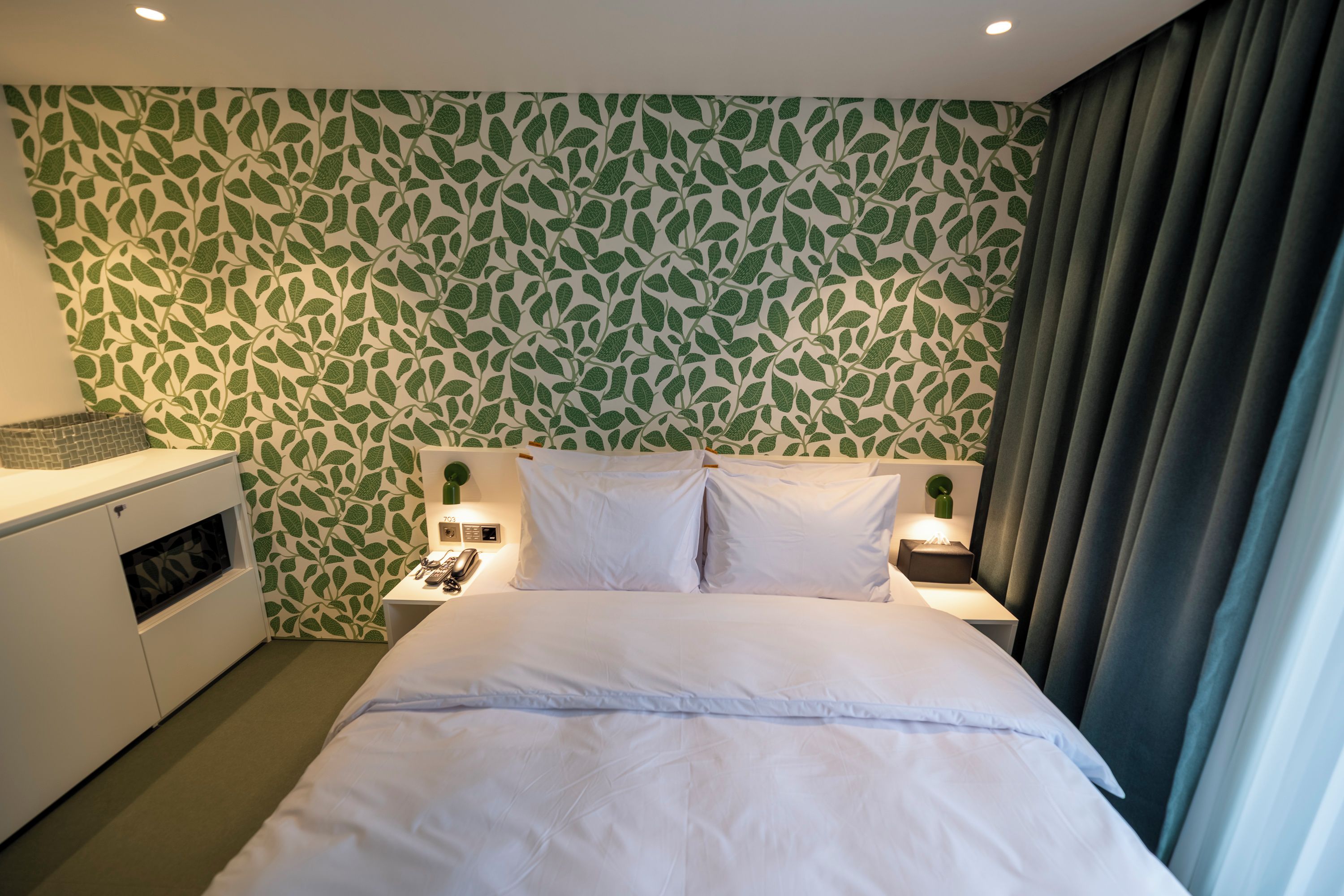 Une chambre d’hôtel avec un lit, des tables de chevet, un téléphone et un mur orné d’un motif de feuilles.
