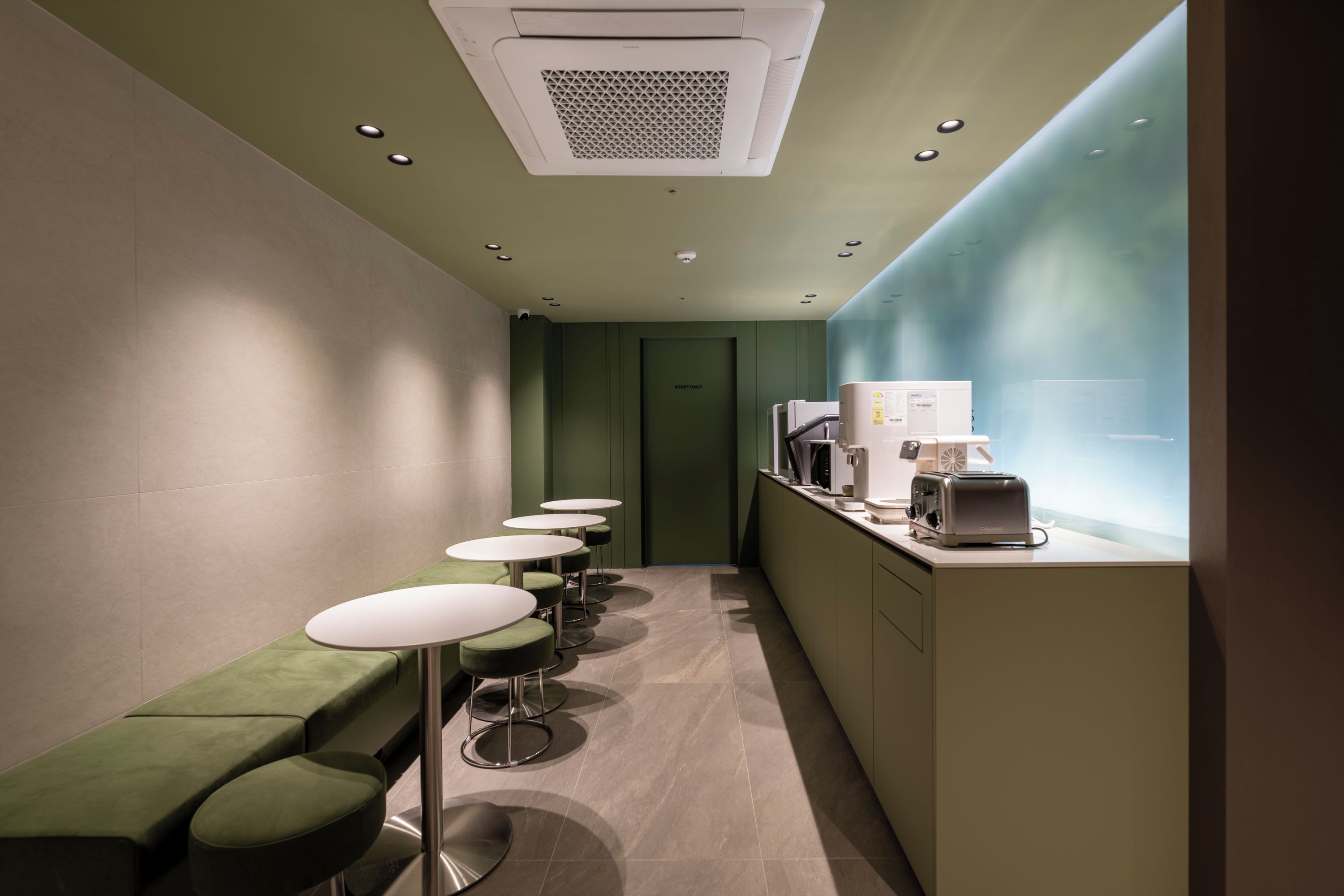 Un pasillo estrecho con asientos verdes, una kitchenette y una puerta que indica 'PERSONAL AUTORIZADO'.