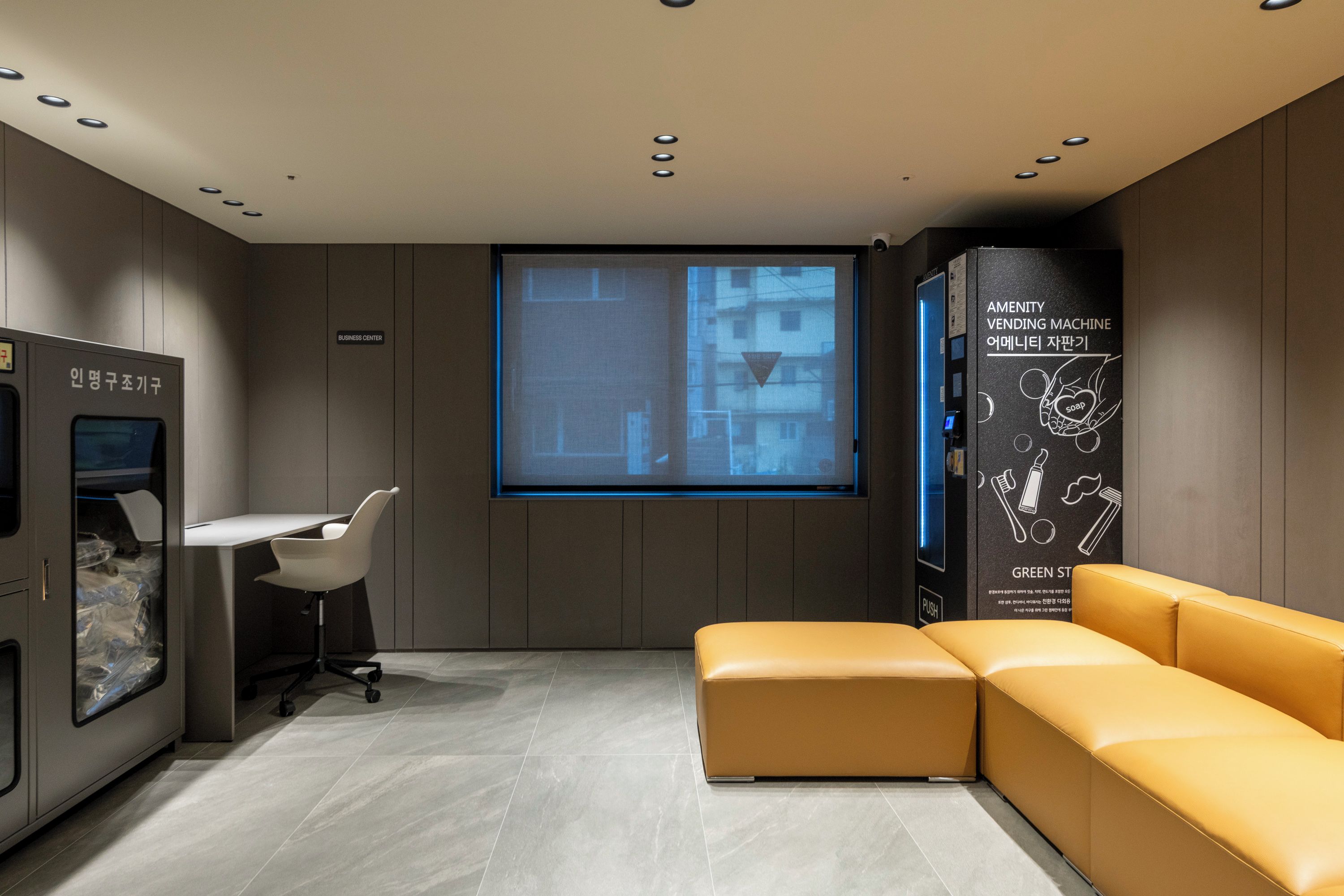 A modern interior with a sofa, a desk, a vending machine, and a projection screen.