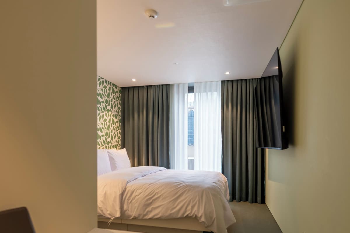 A hotel room with a bed, a desk, a chair, a TV, and a window with curtains.
