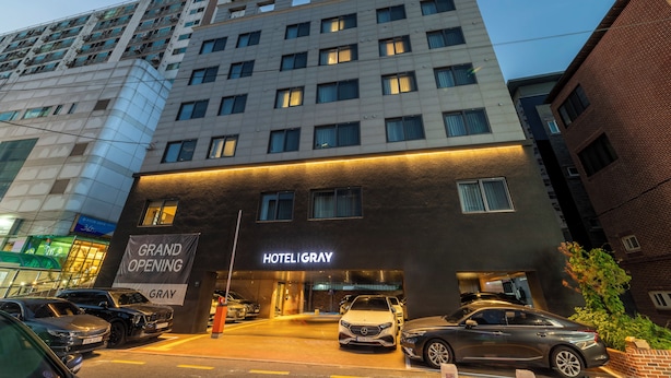 A hotel with a modern facade, multiple floors, and a prominent entrance with a sign indicating a grand opening. - Gray Hotel (Yongin)